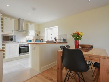 A kitchen with white cabinets and a wooden dining table with black chairs a vase with flowers at Rock Lodge in Alnmouth