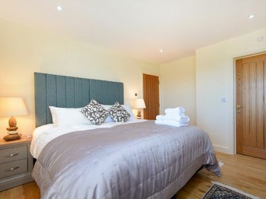 A bedroom with a gray padded headboard bed two bedside tables with lamps and wooden doors at Rock Lodge in Alnmouth