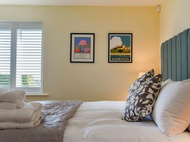 A bedroom with a bed with patterned pillows folded towels on bed and framed pictures on wall at Rock Lodge in Alnmouth