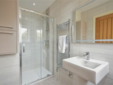 A bathroom with a glass shower enclosure a white sink a towel rail with a white towel and a wooden door at Rock Lodge in Alnmouth