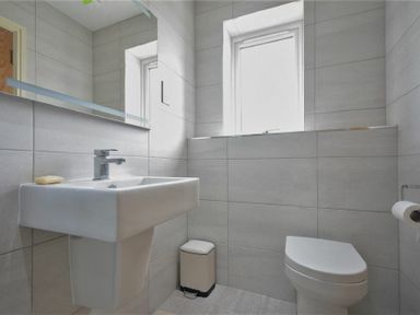 A bathroom with a wall-mounted sink and faucet a window a toilet and a waste bin at Rock Lodge in Alnmouth