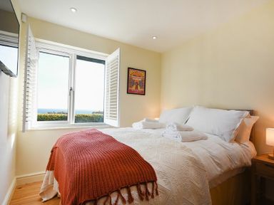 A bedroom with a double bed covered with white linens and an orange throw near a window with white shutters at Rock Lodge in Alnmouth