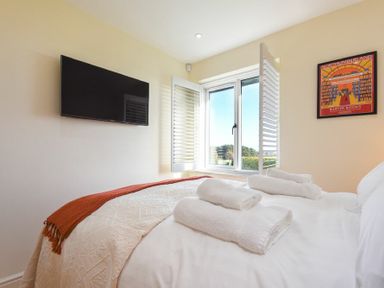 A bedroom with a bed with white linens and towels a wall-mounted television and a window with shutters at Rock Lodge in Alnmouth