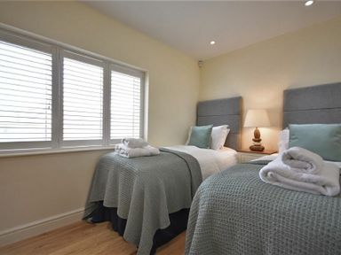 A bedroom with two single beds a bedside table with lamp and window with shutters at Rock Lodge in Alnmouth
