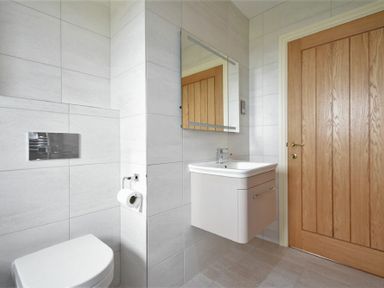 A bathroom with a wall-mounted toilet and sink a mirror above the sink and a wooden door at Rock Lodge in Alnmouth