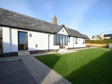 A single story house with white walls slate roof patio and lawn at Rock Lodge in Alnmouth