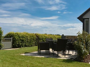An outdoor patio with a table and chairs on a lawn by a house at Rock Lodge in Alnmouth