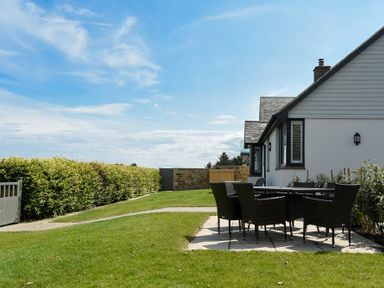 A garden with a patio table and chairs next to a white house at Rock Lodge in Alnmouth
