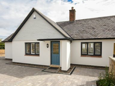 Front view of a single-story house with a blue door and two windows with shutters at Rock Lodge in Alnmouth