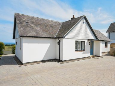 A white house with a grey tiled roof and a blue door on a paved driveway at Rock Lodge in Alnmouth