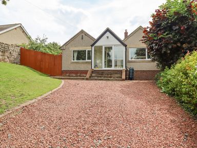 A front view of a house with a gravel driveway lawn on the left and bushes on the right at Manor Cottage in Embleton