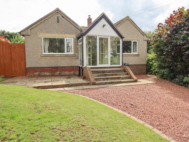 A single story house with a glass porch entrance steps lawn and gravel area at Manor Cottage in Embleton