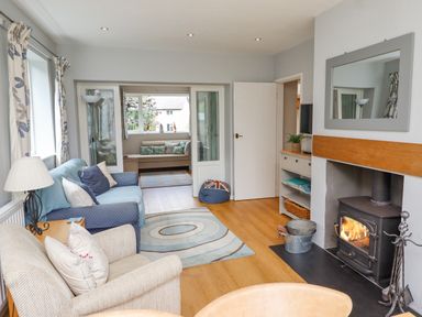 A living room with armchairs a wood burning stove a rug and a connecting smaller seating area at Manor Cottage in Embleton