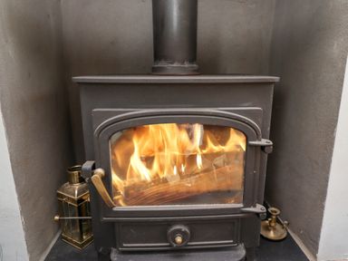 A wood burning stove with fire inside and brass candle holders beside it at Manor Cottage in Embleton