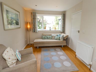 A small living room with a beige sofa and armchair cushions a polka dot rug floor lamp and window at Manor Cottage in Embleton
