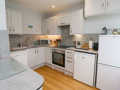 A kitchen with white cabinets, a microwave, oven, sink, dishwasher, small refrigerator, and countertop appliances at Manor Cottage in Embleton