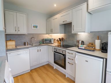 A kitchen with white cabinets dishwasher oven microwave and small fridge at Manor Cottage in Embleton