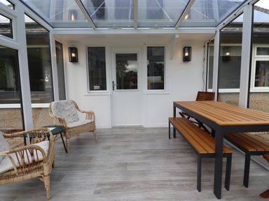 A conservatory with wicker chairs and a wooden dining table with benches at Manor Cottage in Embleton
