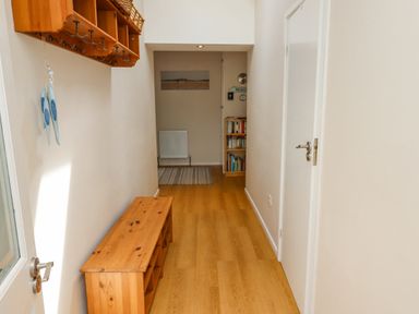 A narrow hallway with wooden flooring and a wooden bench with cubby holes at Manor Cottage in Embleton