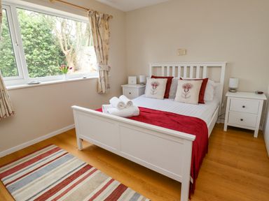 A bedroom with a bed with red and white pillows and blanket two white bedside tables with lamps and a striped rug on the floor at Manor Cottage in Embleton