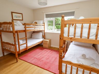 A bedroom with two wooden bunk beds a window two bedside tables and a red rug at Manor Cottage in Embleton
