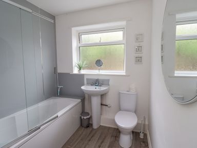A bathroom with a bathtub shower sink toilet mirror and small plant at Manor Cottage in Embleton