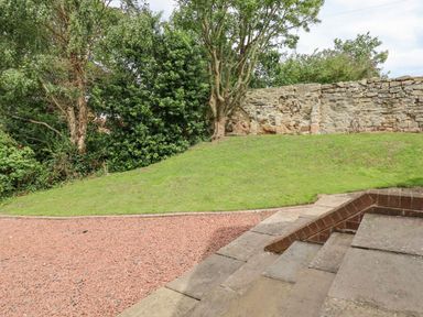 An outdoor area with stone steps, gravel path, grass hill, trees, and a stone wall at Manor Cottage in Embleton