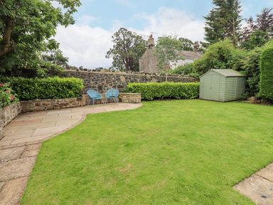 A garden with green grass a stone wall two blue chairs and a green shed at Manor Cottage in Embleton