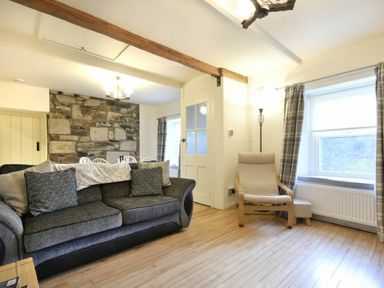 A living room with a gray sofa pillows a wooden armchair near a window and a stone wall at West End Cottage in Embleton