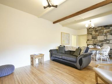 A living room with a grey sofa a wooden side table a blue knitted pouf and a dining table with chairs near a stone wall at West End Cottage in Embleton