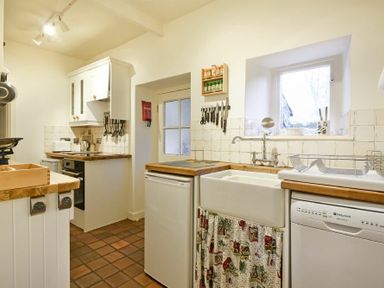 A kitchen with a sink dishwasher fridge oven and wooden countertops at West End Cottage in Embleton