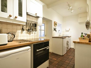 A kitchen with wooden countertops white cabinets hanging utensils and small appliances at West End Cottage in Embleton