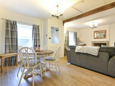 A dining area with a round wooden table and white chairs next to a living room with sofas and a fireplace at West End Cottage in Embleton