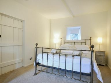 A bedroom with a metal bed frame two bedside tables two lamps and a small window at West End Cottage in Embleton