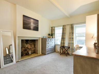 A bedroom with a fireplace a dresser two windows with plaid curtains and a mirror at West End Cottage in Embleton