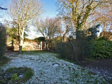 A garden with trees shrubs and a grass lawn with a light dusting of snow at West End Cottage in Embleton
