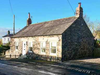 A stone cottage with two chimneys and white framed windows on a street at West End Cottage in Embleton