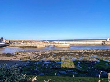 A harbor with boats docked near a concrete pier under a clear blue sky at The Bolthole in Seahouses
