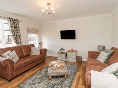 A living room with two brown sofas a wall-mounted TV a patterned rug and a checkered ottoman at The Bolthole (Seahouses) in Seahouses