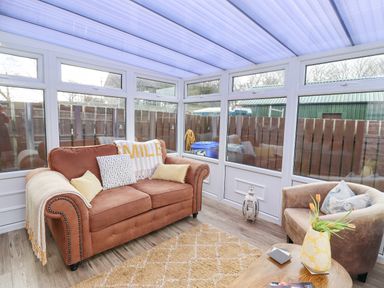 A sunroom with a brown sofa and armchair a wooden coffee table and windows overlooking a fenced yard at The Bolthole Seahouses