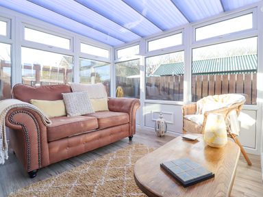 A sunroom with a brown sofa and wicker chair a wooden coffee table and large windows at The Bolthole (Seahouses) in Seahouses