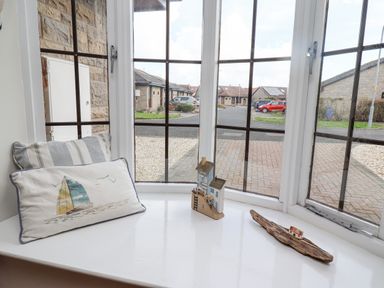A window with a striped cushion a sailboat pillow and small wooden house decorations at The Bolthole in Seahouses