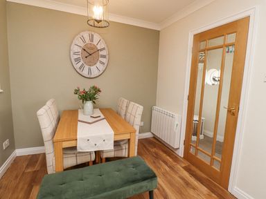 A dining area with table, chairs, bench, clock on wall, and wooden door at The Bolthole (Seahouses) in Seahouses