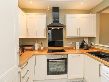 A kitchen with white cabinets wooden countertops electric stove oven toaster kettle and sink at The Bolthole (Seahouses) in Seahouses