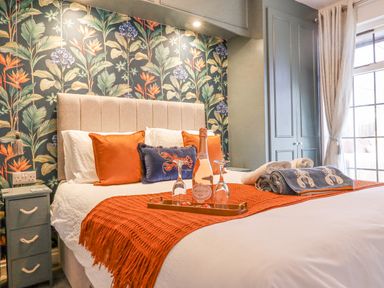 A bedroom with a bed with orange pillows and blanket a bottle of prosecco on a tray and towels on the bed at The Bolthole Seahouses