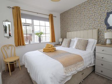 A bedroom with a bed two bedside tables and a window with yellow curtains at The Bolthole (Seahouses) in Seahouses