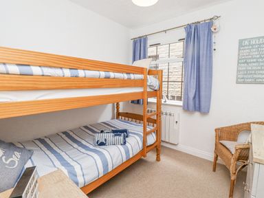 A bedroom with wooden bunk beds striped bedding a wicker chair and blue curtains at The Bolthole (Seahouses) in Seahouses