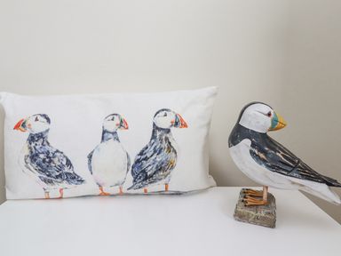 A pillow with puffin illustrations and a puffin figurine on a white surface at The Bolthole Seahouses