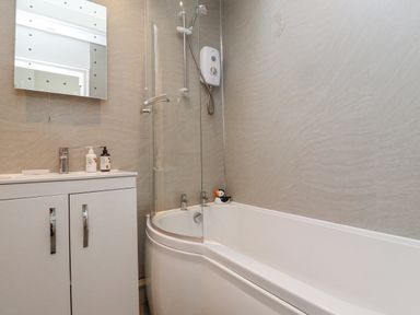 A bathroom with a bathtub and shower combination a sink with a cabinet and a mirror at The Bolthole (Seahouses) in Seahouses