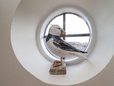 A round window with a wooden bird decoration on the windowsill at The Bolthole (Seahouses) in Seahouses